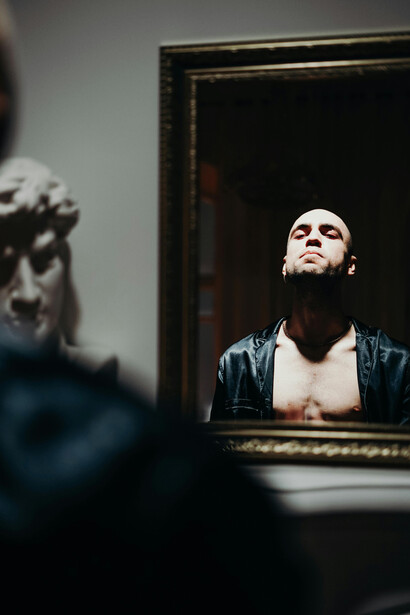 Man holding his face while staring into a mirror, reflecting an identity crisis
