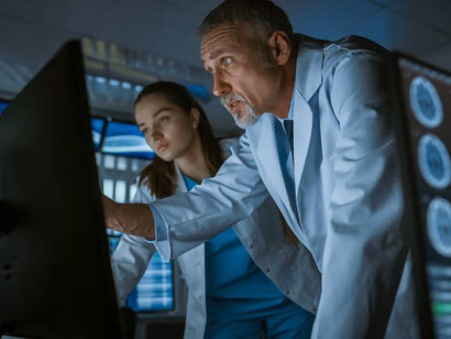 Two neurophysiologists are closely examining a brain scan displayed on screens