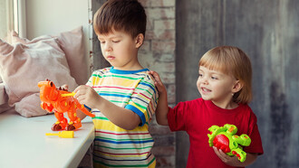 Duas crianças brincam uma ao lado da outra com dinossauros de brinquedo