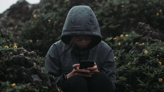 A person sitting on a rock, staring at their phone, surrounded by a sense of grief and the haunting presence of technology