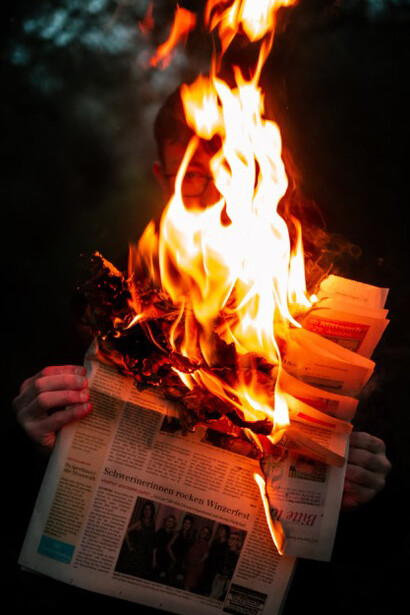 The image of a person holding a burning newspaper reflects the destructive impact of information pollution and media manipulation, highlighting the urgent need for democratic resilience