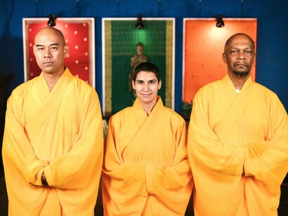 Three monks posing with a statue of a buddha behind them
