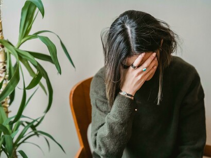 Distressed woman sitting on a chair with her knees pulled in, overwhelmed by negative thoughts