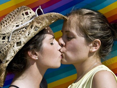 Dos mujeres se besan delante de la bandera del arcoíris