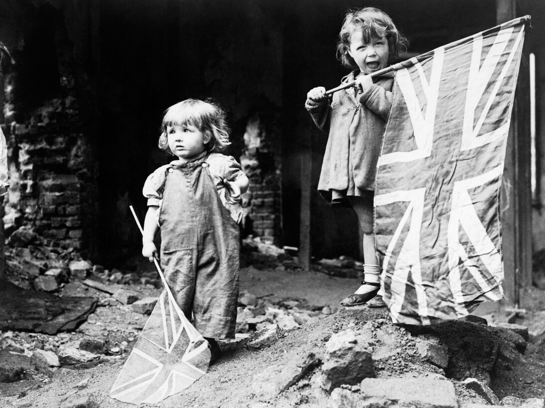 Two small girls waving their flags to celebrate the end of the war in the rubble of Battersea on VE Day