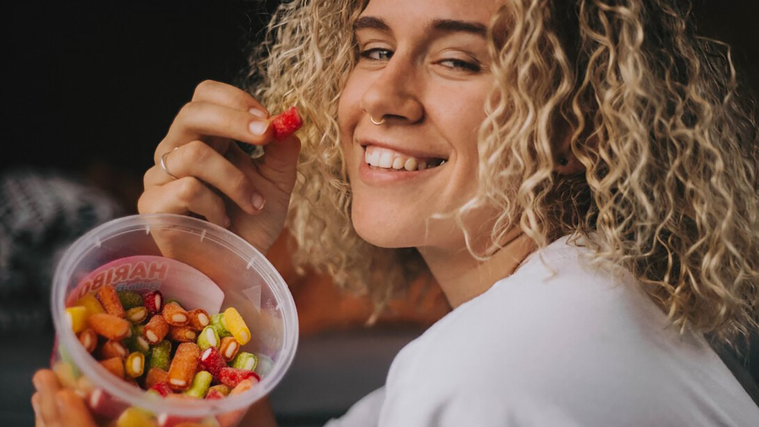 A woman in a white long-sleeve shirt holding a clear plastic container filled with colorful candies