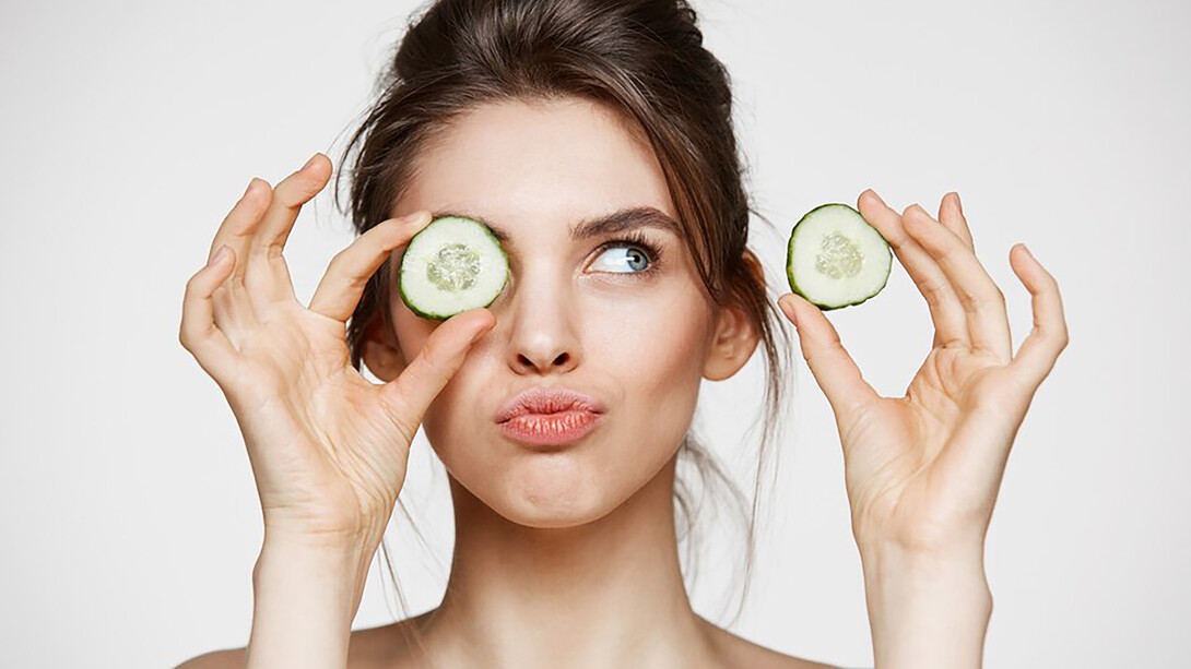 A woman in a tranquil spa setting, gently placing cucumber slices over her eyes, surrounded by luxurious skincare products like creams and oils