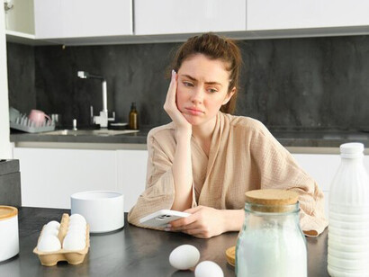 A girl baking in the kitchen, preparing dough with a recipe book in hand, surrounded by milk and butter for cakes and cookies