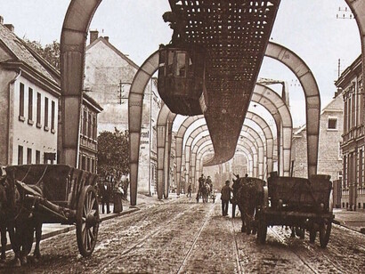 Die Schwebebahn fährt in Sonnborn. Unten auf der Fahrbahn waren offene Güterwagen noch von Pferden gezogen, ca. 1903 (Siehe Cover, mittig)