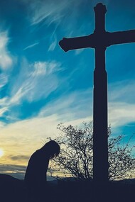 A person kneeling before a cross on a hill, representing a return to sincere and humble faith