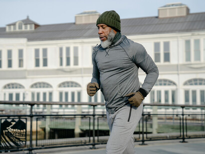 A bearded man dressed for cold jogging near a river