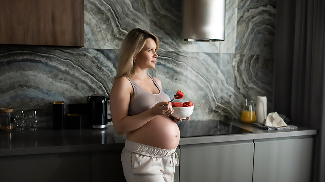 A medium shot of a pregnant woman enjoying a fruit bowl, emphasizing the benefits of nutritious food choices during pregnancy for both mother and baby