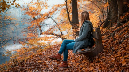 A woman sitting quietly on a bench surrounded by autumn leaves, representing the beauty of embracing a slower, simpler life