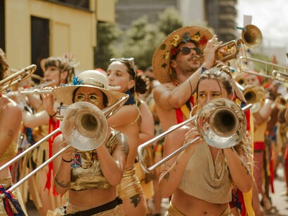 Bloco de rua. Em Pinheiros, Miguel, trajando terno, esquenta o bloco com alguns comandos para os ritmistas. A Mariana, em seu tailleur, está eufórica. É seu primeiro ano na bateria do bloco. De tanto o seu diretor comentar sobre a experiência, resolveu experimentar, entrou nos ensaios ao longo do ano anterior e aquele momento era o seu Grand-debut. Ansiava que o Cadu chegasse logo para que pudesse vê-la. Há quase um ano nutria uma paixão platônica por ele e acreditava que aquele momento de descontração poderia ser ideal para deslanchar um possível romance