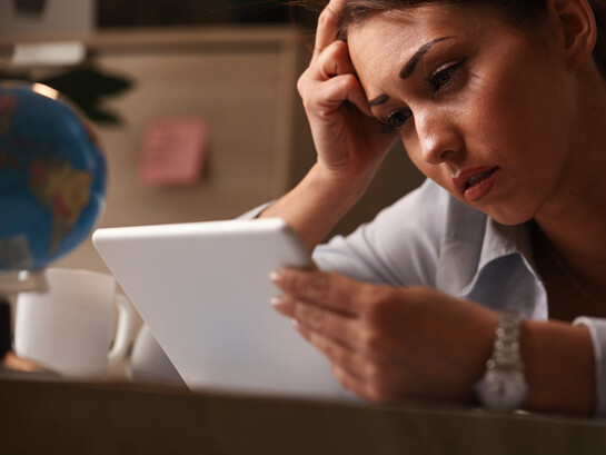 A young woman at work reacting with sadness as she reads on her touchpad