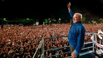 De uma plataforma, Luiz Inácio Lula da Silva ergue o braço em saudação a uma multidão que ocupa a rua e o espaço público durante a noite. Milhares de pessoas levantam as mãos e os celulares, enquanto bandeiras e manifestações de apoio compõem a cena. A imagem traduz a dimensão popular da vitória de Lula e a capacidade de mobilização que marcou sua trajetória política. Para Boaventura de Sousa Santos, porém, a vitória eleitoral não encerra a disputa em torno do futuro do Brasil: ela recoloca no centro do debate a defesa da democracia, o enfrentamento da extrema-direita e a tarefa de transformar o apoio popular em participação política efetiva