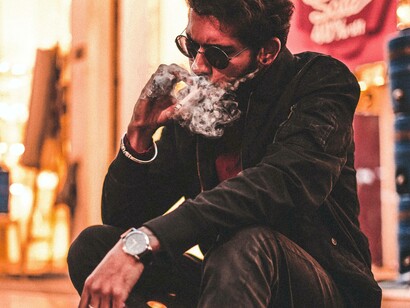 A man takes a long puff from his cigarette as smoke escapes his mouth