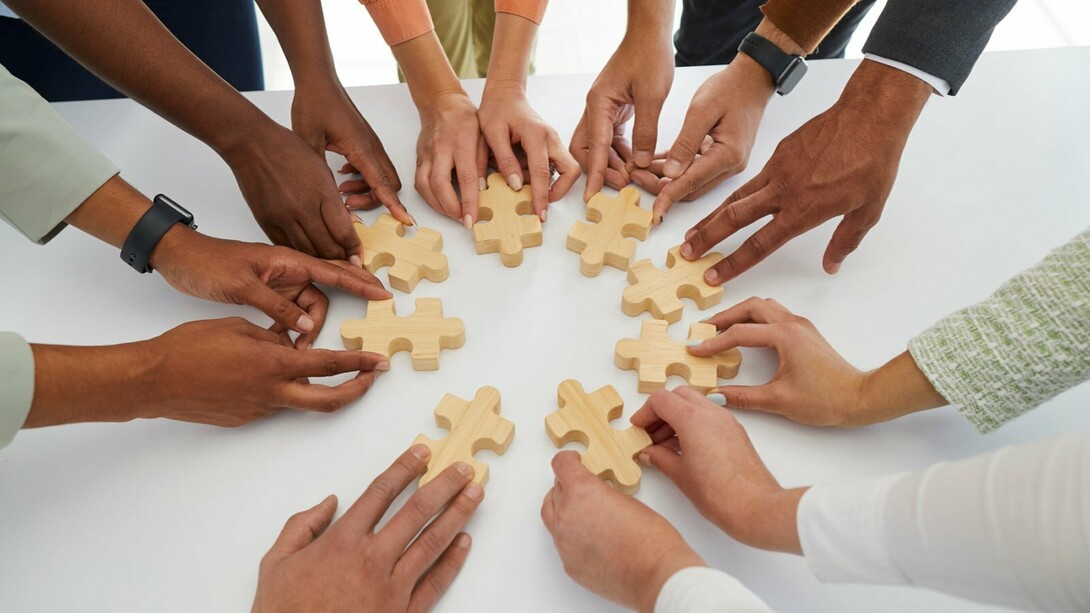 Mãos de diferentes pessoas movimentam peças de um quebra-cabeça sobre uma mesa. A construção coletiva de soluções está no centro da atuação do terceiro setor, que articula pessoas, recursos e competências em torno de objetivos sociais