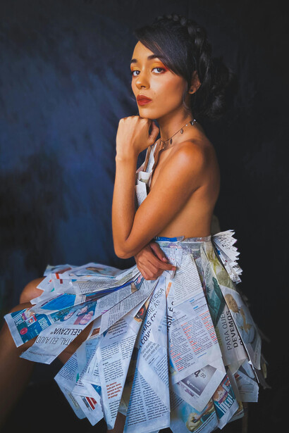 Sitting on the floor in a newspaper dress, a woman represents eco-friendly fashion, emphasizing upcycling and the use of biodegradable materials