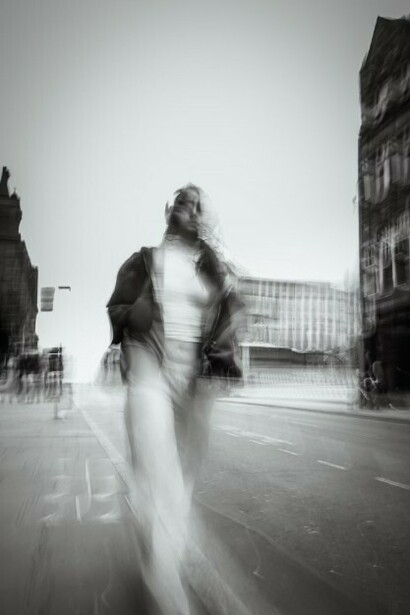 A blurred black and white photo of a woman walking alone along a city street
