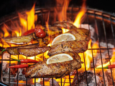 Grilled chicken breast on the flaming grill with Grilled vegetables tomatoes, herbs, lemon, rosemary