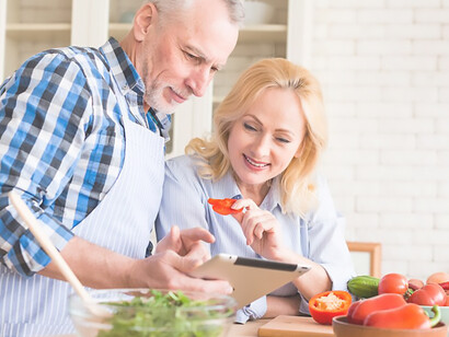 Elevate longevity by showcasing a senior couple engaged in antioxidant-rich Mediterranean diet practices, using a digital tablet while preparing a nutritious salad in the kitchen