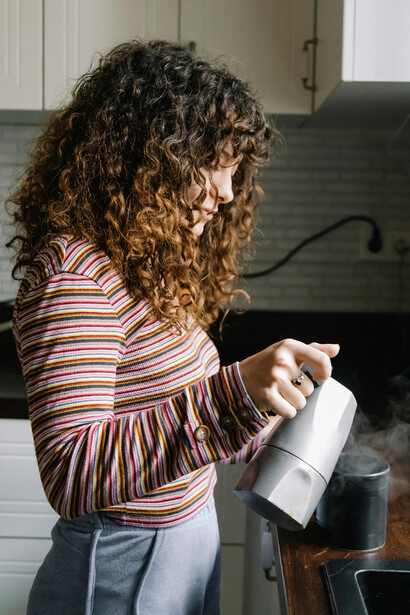 A woman prepares coffee in a quiet kitchen with soft, natural lighting