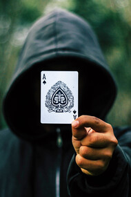 A man in a black hooding holding the ace of spades