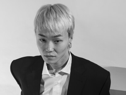 Black-and-white medium portrait of a young man posing against an empty background, creating a minimalist and introspective atmosphere