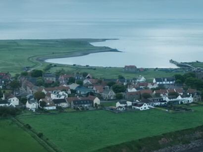 A quiet coastal village surrounded by green fields, symbolizing humanity’s determination to rebuild after catastrophe