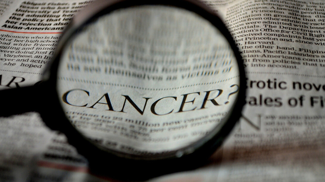 Beneath the magnifying glass, the word 'cancer' becomes apparent on the newspaper