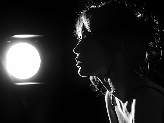 A silhueta de uma mulher emerge diante de uma única luz, enquanto o resto permanece em sombra. Em “Joshua”, Elsa Mangue transforma esse contraste entre escuridão e claridade numa recusa que também é sobrevivência. A imagem ecoa a força íntima de quem fecha a porta para não morrer por dentro