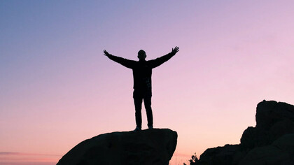 Un uomo alza le mani al cielo su una montagna al tramonto