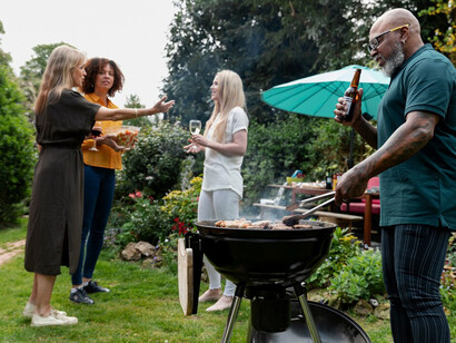 A family enjoying a barbecue together, with a man tending to the grill as flames flare up from the charcoal