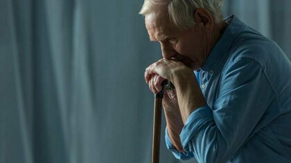 Un uomo si appoggia al proprio bastone pensieroso