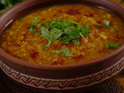 Against a rustic black wooden background, a tantalizing bowl of traditional Indian dal, featuring a spicy lentil curry, takes center stage, complemented by an assortment of aromatic spices and herbs