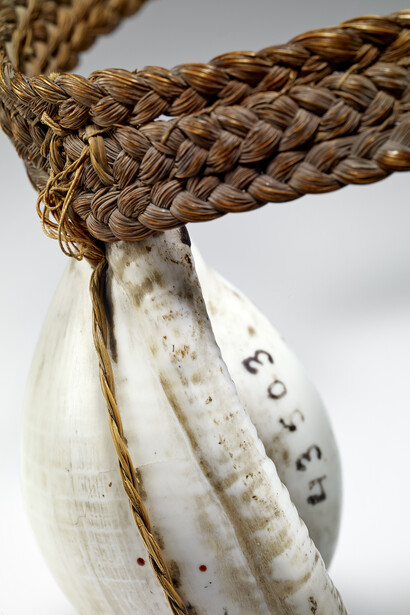 Anneau (ouvert) de fibres végétales tressées sur lequel est accroché, à l'aide d'un lien en fibres, un coquillage poli © musée du quai Branly, photo Claude Germain