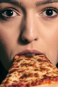 A woman looks shocked as she takes a bite of a slice of pizza