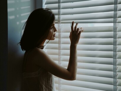 Woman gazing through hospital window as sunlight filters through the shutters
