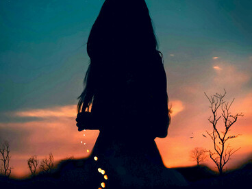 Silhouetted against the moonlit sky, a lone person looks up at the stars while a luminous path winds through the twilight landscape