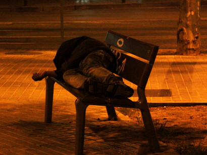 Hombre sin hogar duerme en una banca en la calle