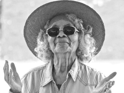 A cheerful elderly woman in sunglasses and a hat