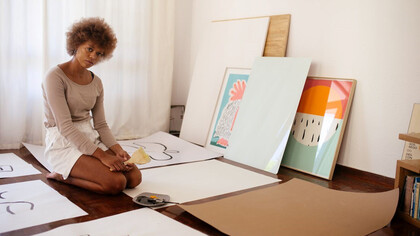 A young artist sitting on the floor surrounded by their artworks