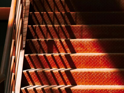 Escalier rouge traversé par un rayon de soleil, créant une ombre qui pourrait représenter l'illusion liée à la reconnaissance comme service