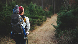 Madre carga su pequeña hija a sus espaldas por un camino campestre