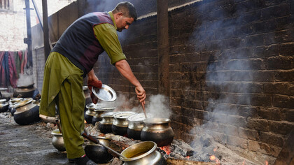 A man stirs food in large pots over an open flame, preparing a traditional meal, Srinagar, India