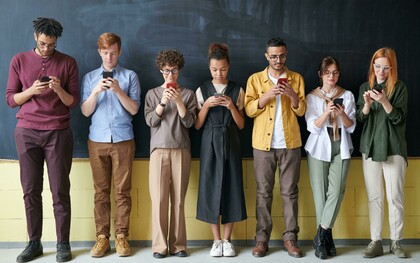 A group of people stands near a blackboard, each focused on their phones instead of the board