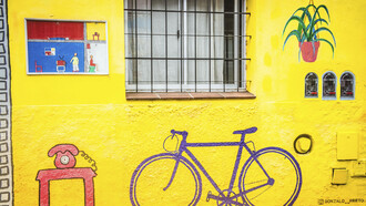Bicicleta en el mural del artista Gonzalo Prieto, pintado en 2020, en el que se muestran las distintas partes de una casa en un vibrante color amarillo
