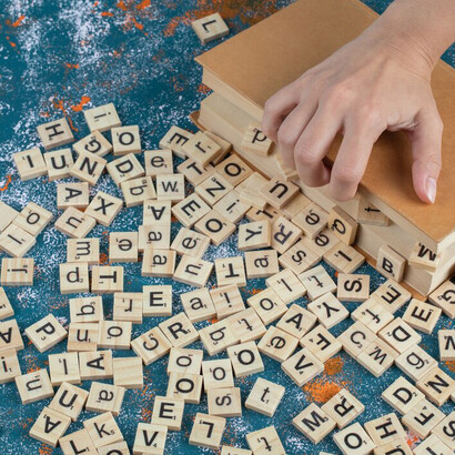 Wooden letters bearing printed letters lie between the pages of a book, illustrating the evolution of language
