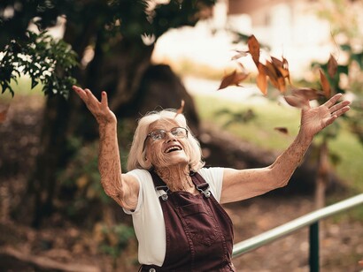 An elderly woman throwing leaves in the air as a symbol of how she approaches life